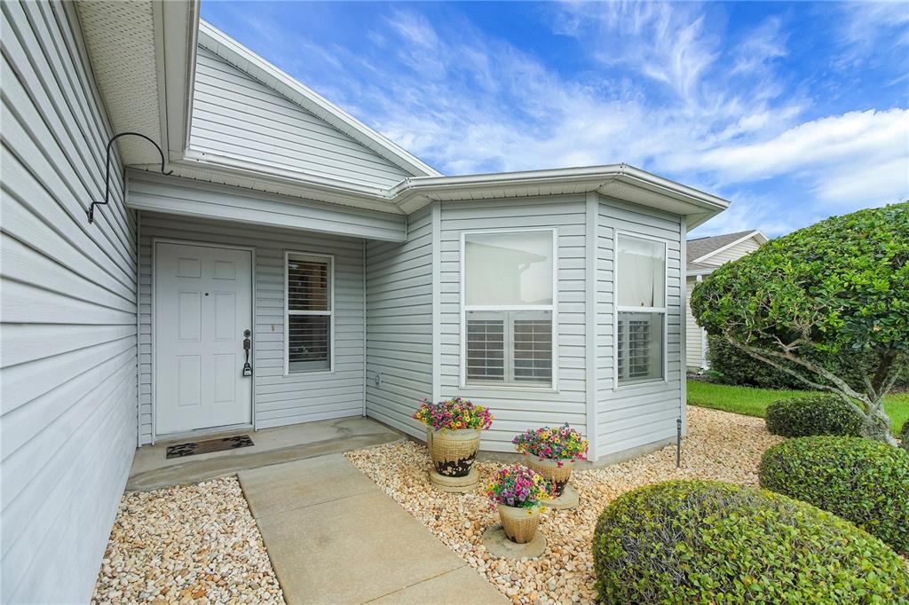 A light gray vinyl-sided house exterior features a front door, bay window, and landscaped yard — 909 EAGLES LANDING, LEESBURG, FL