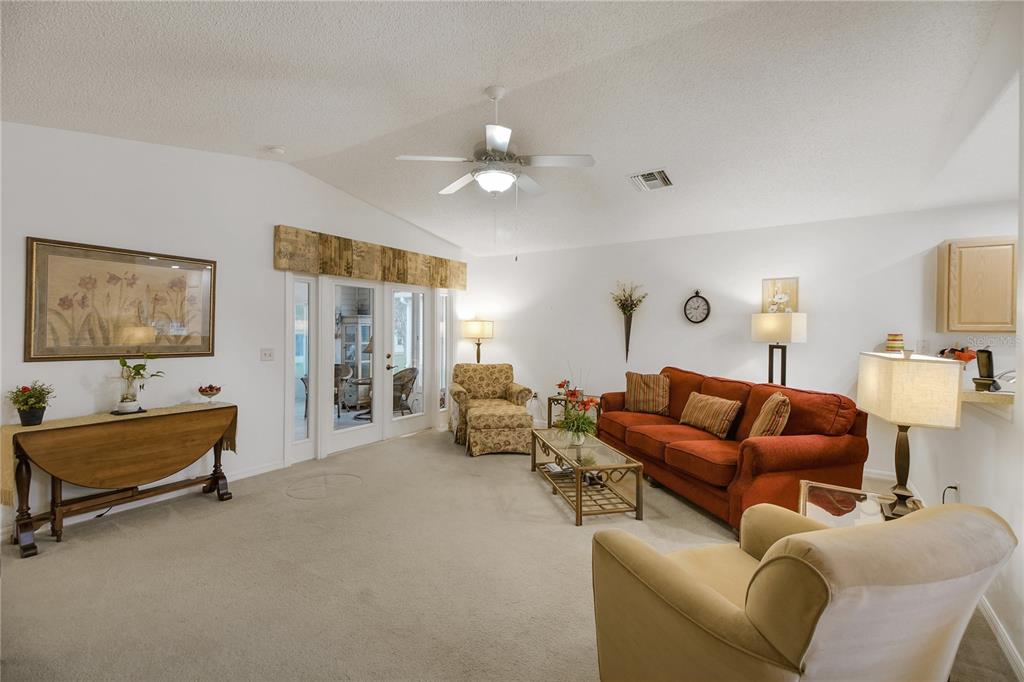 A living room features a vaulted ceiling, beige carpet, a red sofa, and glass patio doors — 909 EAGLES LANDING, LEESBURG, FL