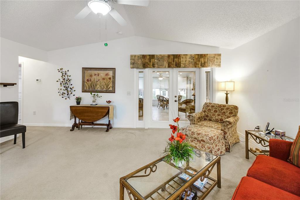 A living room with beige carpet, a glass coffee table, and French doors leading outside — 909 EAGLES LANDING, LEESBURG, FL