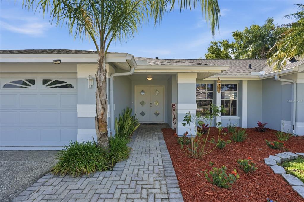 A paved walkway leads to the front entrance of a house with a gray garage — 1775 STABLE TRAIL, PALM HARBOR, FL