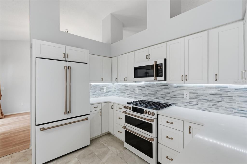 A kitchen features white cabinets, stainless steel appliances, a tiled backsplash, and light-colored countertops — 1775 STABLE TRAIL, PALM HARBOR, FL