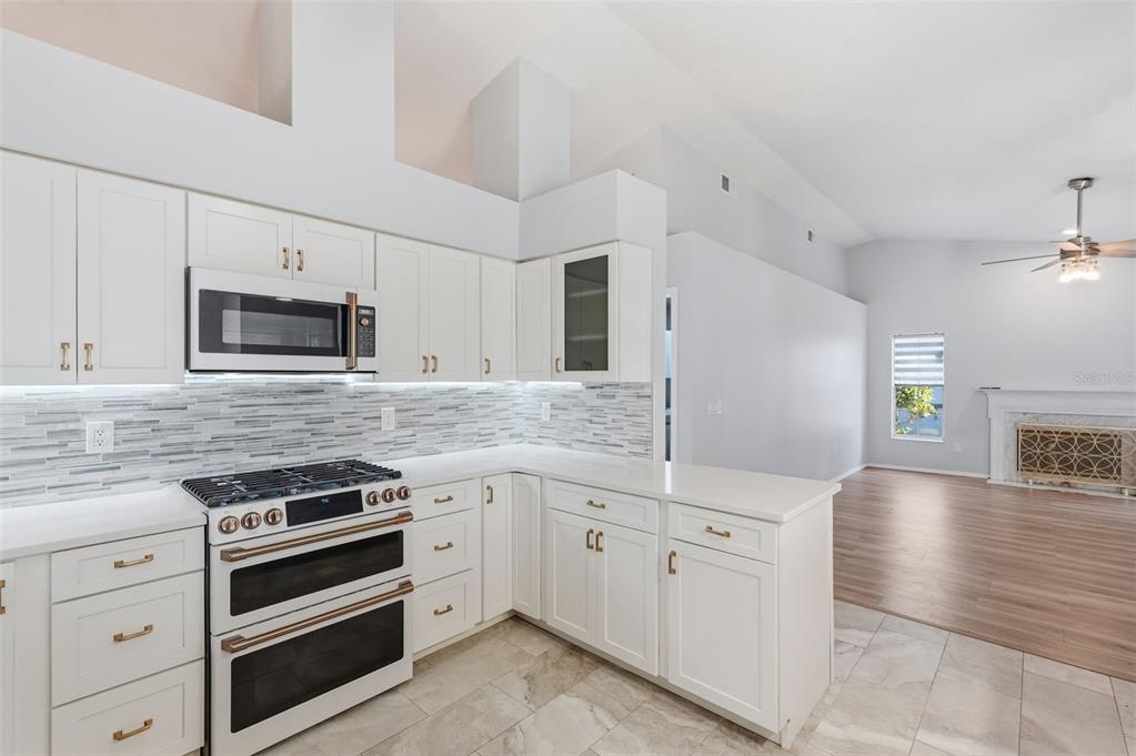 A kitchen with white cabinets, stainless steel appliances, and a tiled backsplash overlooks a living area — 1775 STABLE TRAIL, PALM HARBOR, FL