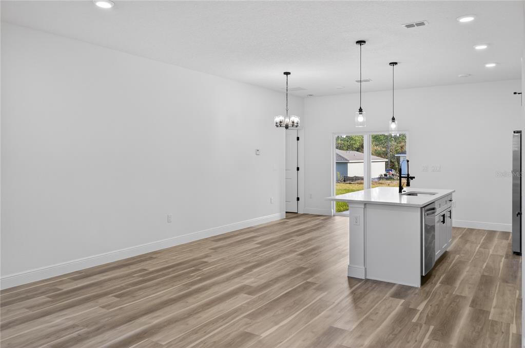 A bright, open-concept kitchen and living area features white walls, wood-look flooring, and a central island — 1852 W QUAKER LANE, CITRUS SPRINGS, FL