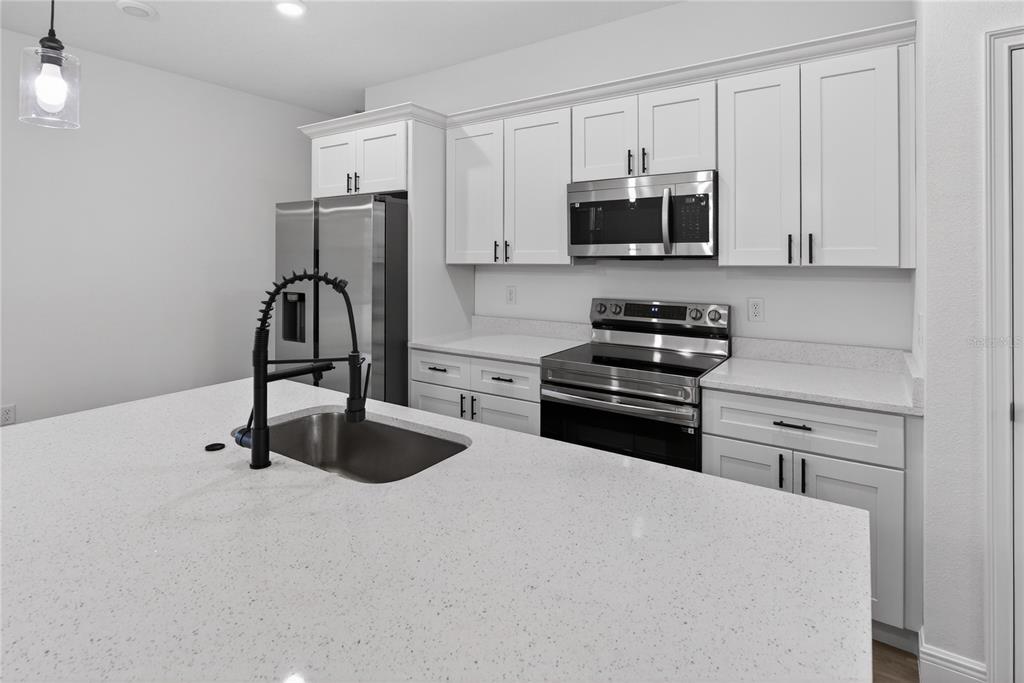 A modern kitchen features white cabinets, stainless steel appliances, and a large quartz-topped island — 1852 W QUAKER LANE, CITRUS SPRINGS, FL