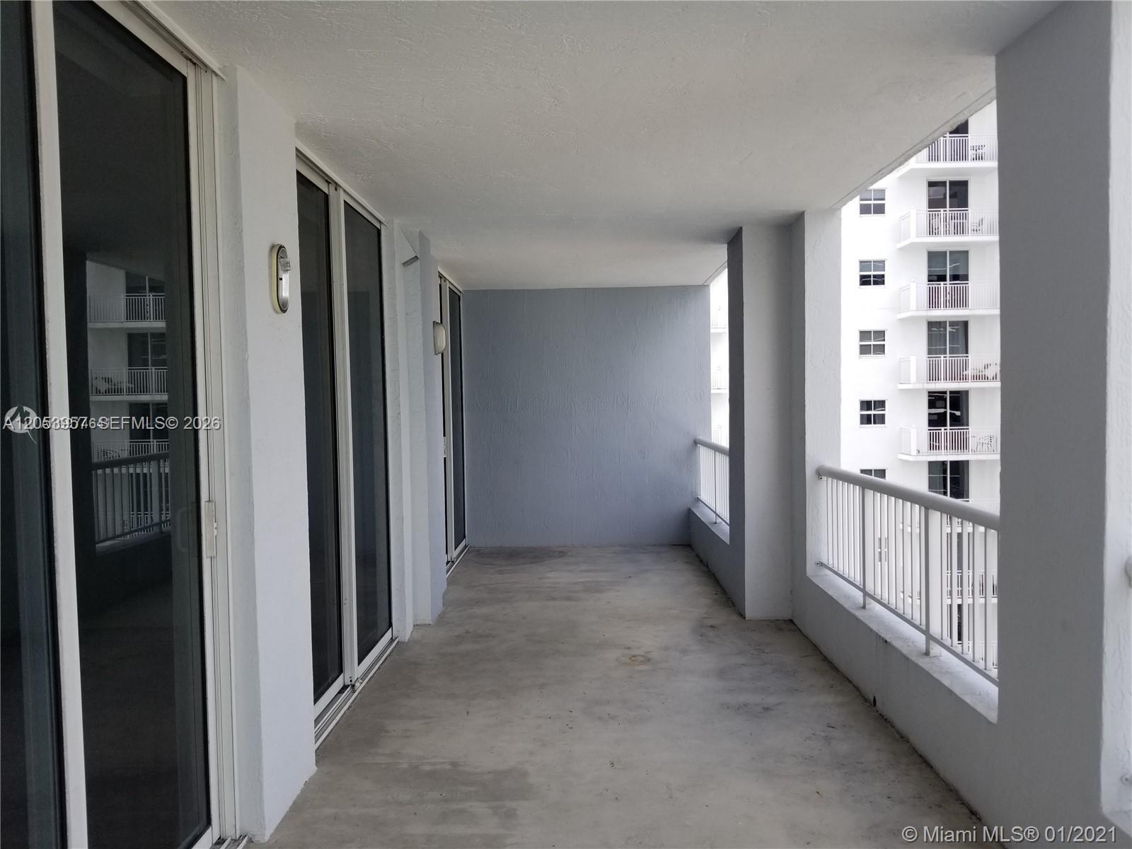 A covered balcony with concrete flooring, white railings, and sliding glass doors — 170 SE 14th St # 2205, Miami FL 33131, MIAMI, FL