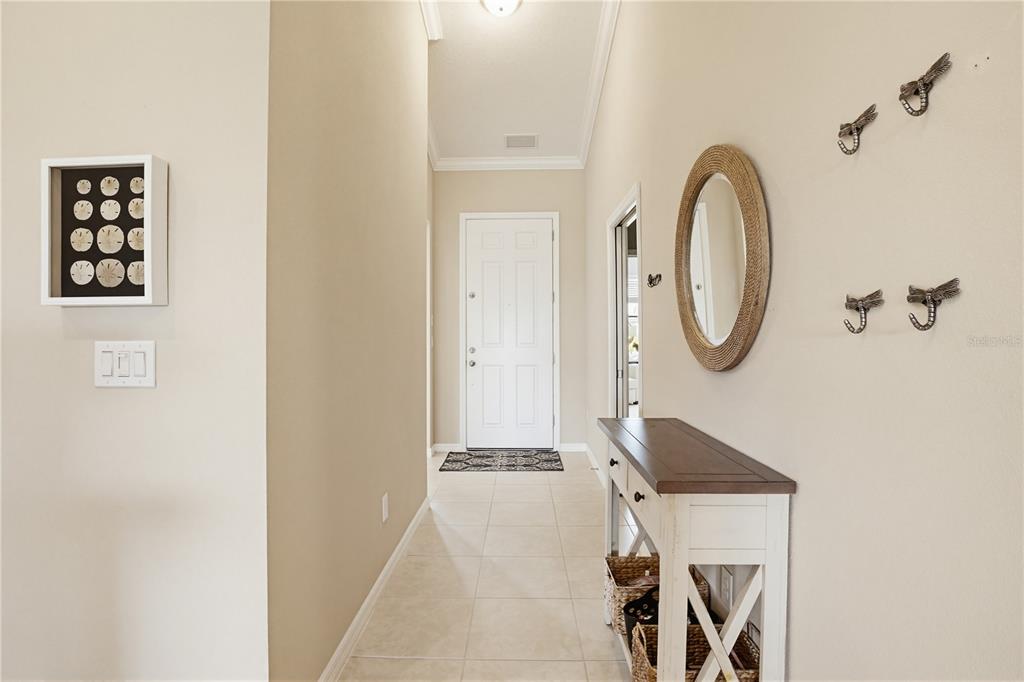 A neutral-toned entryway features a white front door, a console table, and wall-mounted decor — 13810 MESSINA LOOP UNIT 203, BRADENTON, FL