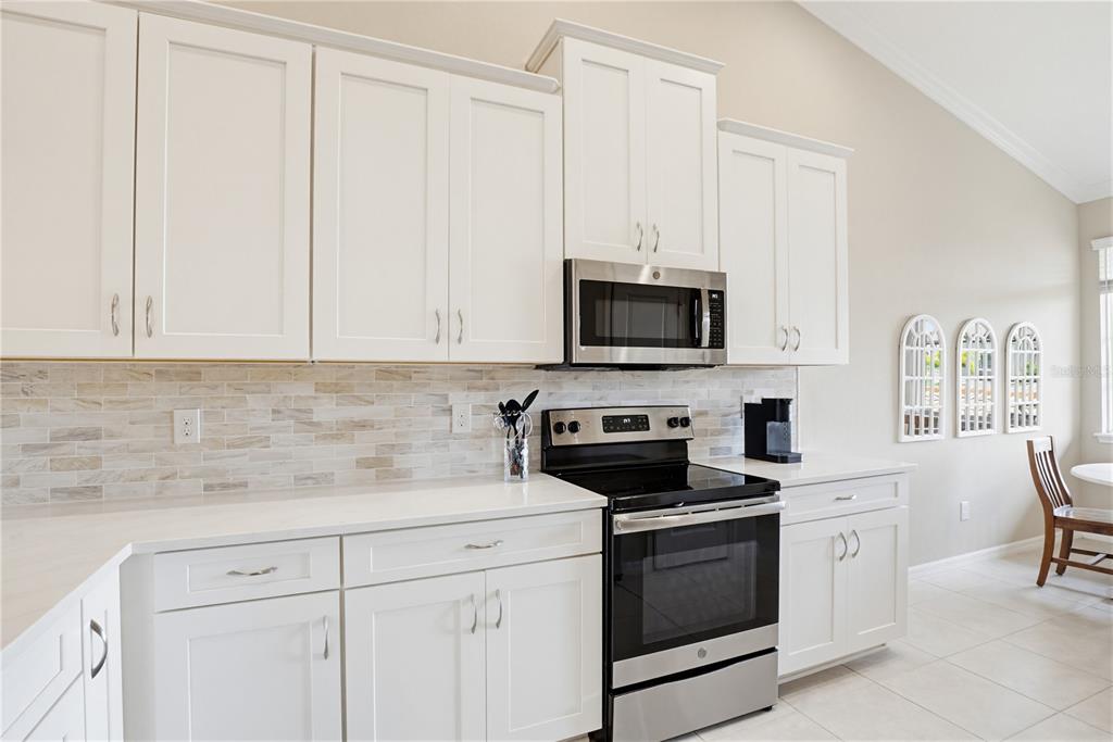 A kitchen features white cabinets, stainless steel appliances, and a light-colored tile backsplash — 13810 MESSINA LOOP UNIT 203, BRADENTON, FL