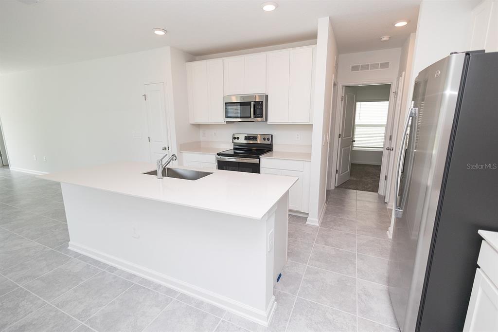 A kitchen features white cabinets, stainless steel appliances, a center island, and light tile flooring — 2165 AQUIFER LANE, DAVENPORT, FL