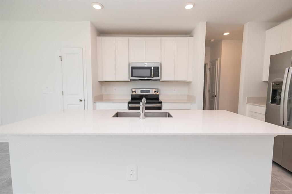 A modern kitchen features white cabinets, stainless steel appliances, and a large central island — 2165 AQUIFER LANE, DAVENPORT, FL