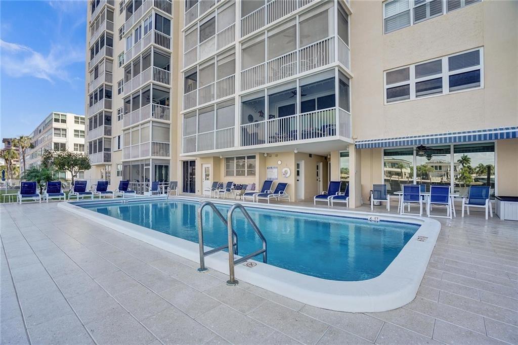 A rectangular swimming pool sits on a tiled patio beside a multi-story apartment building — 303 N Riverside Drive # 4, Pompano Beach FL 33062, POMPANO BEACH, FL