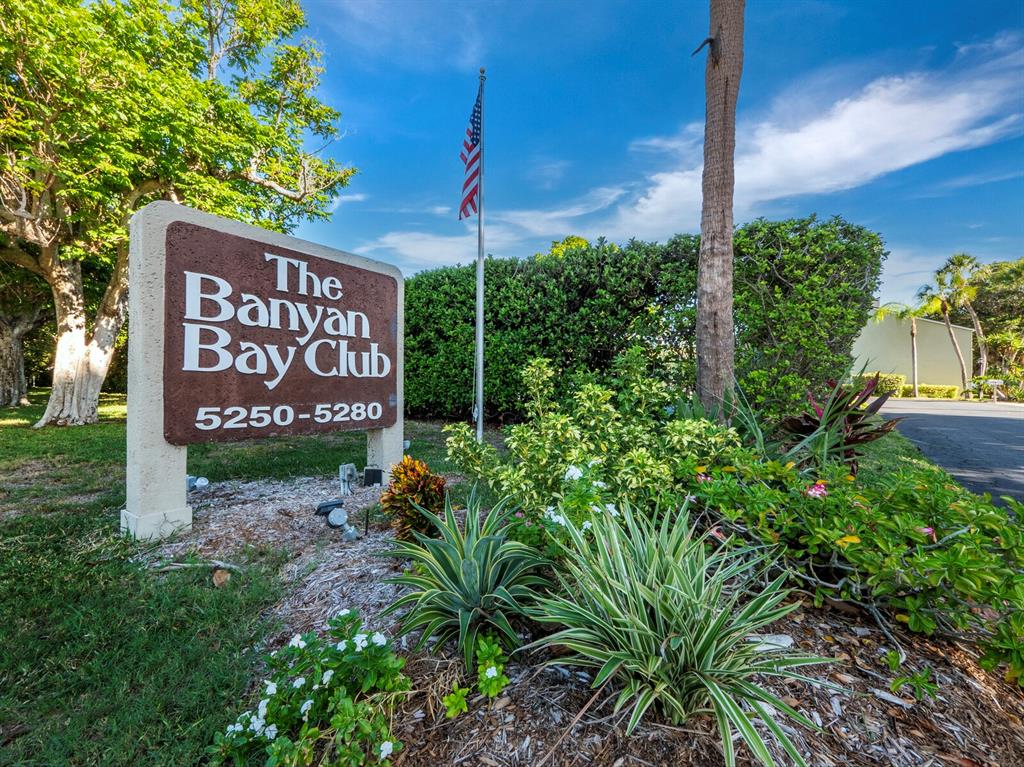 A sign for The Banyan Bay Club stands in a landscaped garden with a flagpole — 5260 GULF OF MEXICO DRIVE UNIT 413, LONGBOAT KEY, FL