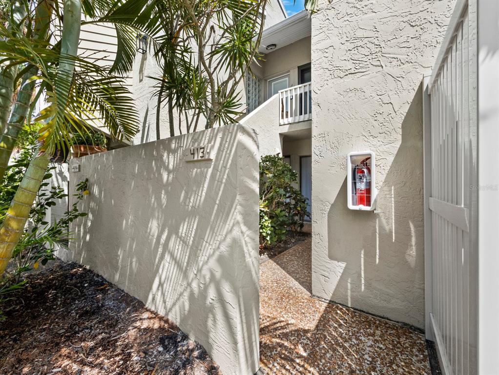 An exterior view shows a beige stucco building entrance with a fire extinguisher and landscaping — 5260 GULF OF MEXICO DRIVE UNIT 413, LONGBOAT KEY, FL