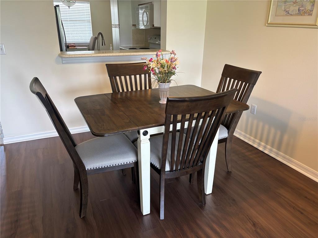 A dining area features a wooden table with white legs and four upholstered chairs — 6507 STONE RIVER ROAD UNIT 105, BRADENTON, FL