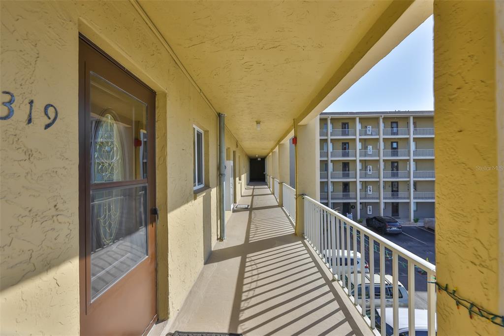 An outdoor apartment walkway with a yellow wall, a brown door, and a metal railing — 3656 LAKE BAYSHORE DR, BLDG K UNIT 319, BRADENTON, FL