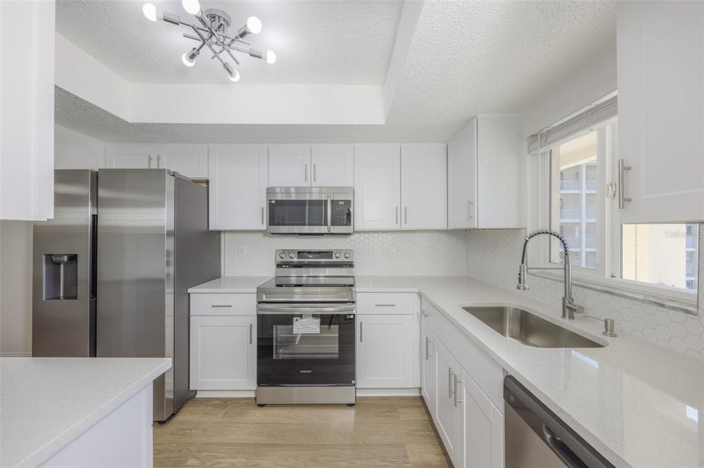 A modern kitchen features white cabinets, stainless steel appliances, and light-colored quartz countertops — 3656 LAKE BAYSHORE DR, BLDG K UNIT 319, BRADENTON, FL