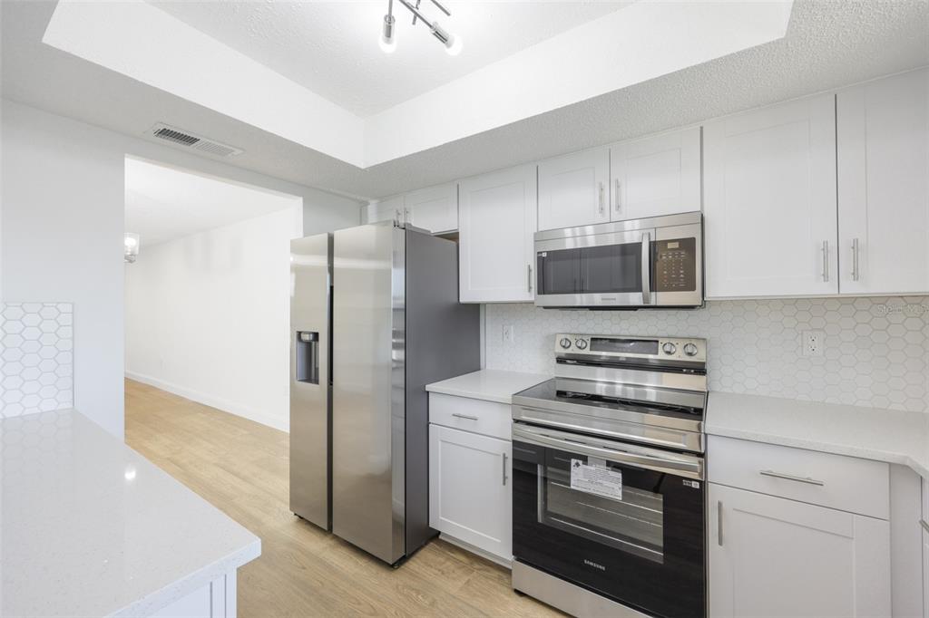A kitchen featuring white cabinets, stainless steel appliances, quartz countertops, and a hexagonal tile backsplash — 3656 LAKE BAYSHORE DR, BLDG K UNIT 319, BRADENTON, FL
