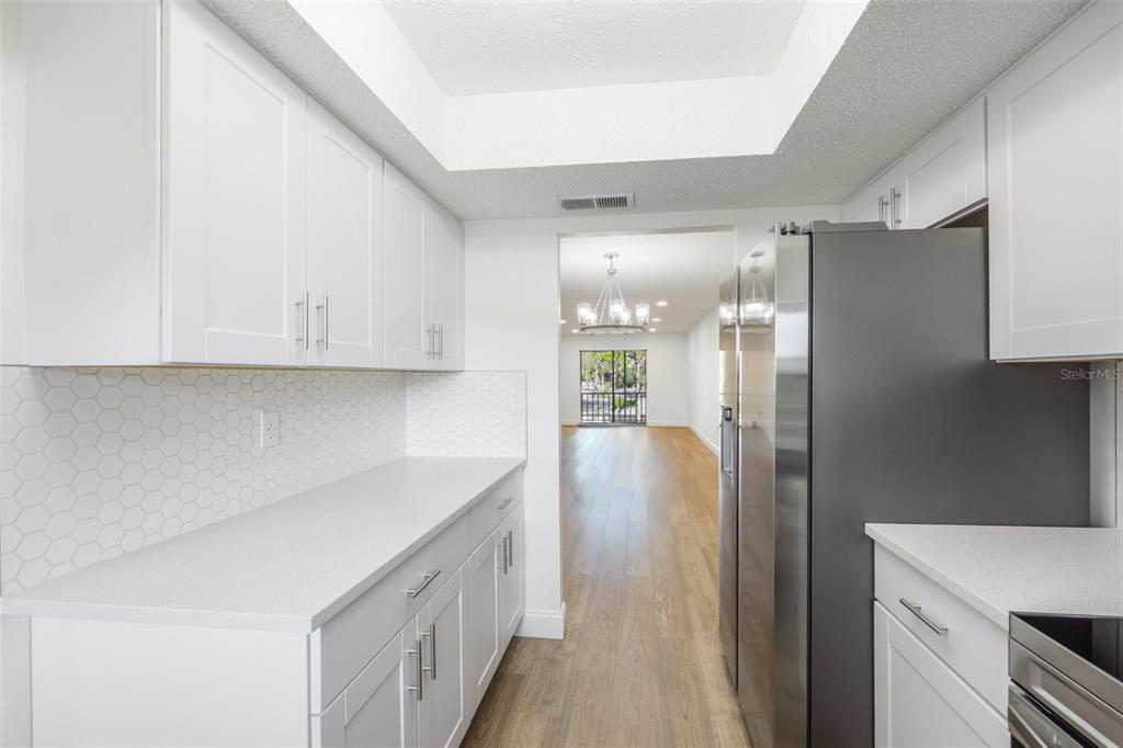 A white kitchen features quartz countertops, a hexagonal tile backsplash, and stainless steel appliances — 3656 LAKE BAYSHORE DR, BLDG K UNIT 319, BRADENTON, FL