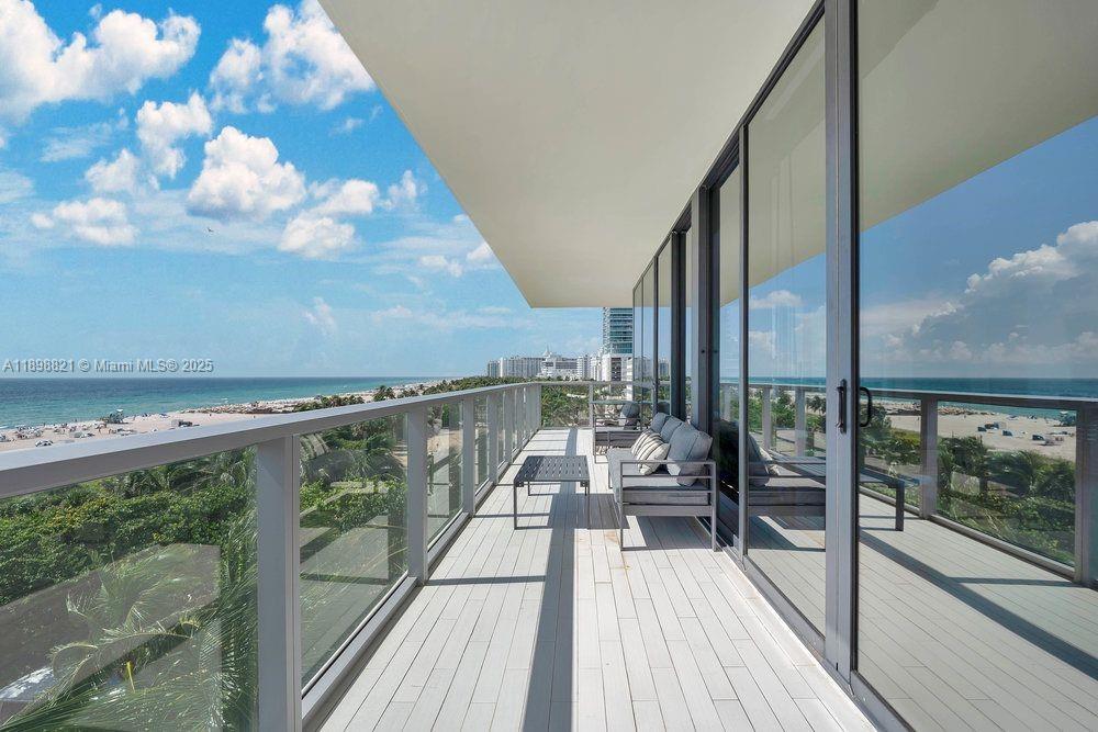 A balcony with a glass railing overlooks a beach and ocean under a blue sky — 2201 Collins Ave # 628, Miami Beach FL 33139, MIAMI BEACH, FL
