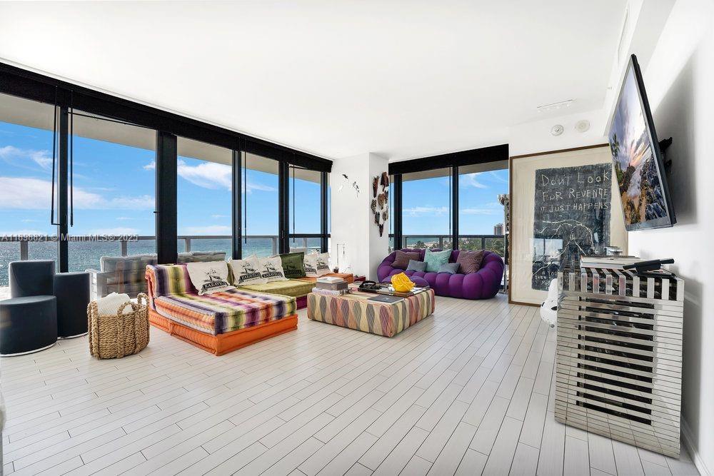 A modern living room features floor-to-ceiling windows, white tile floors, and colorful low-profile furniture — 2201 Collins Ave # 628, Miami Beach FL 33139, MIAMI BEACH, FL