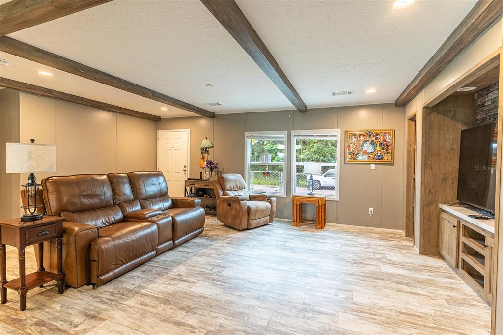 A living room features wood-look tile flooring, exposed ceiling beams, a leather sofa, and a television — 6668 CAIN STREET, MULBERRY, FL