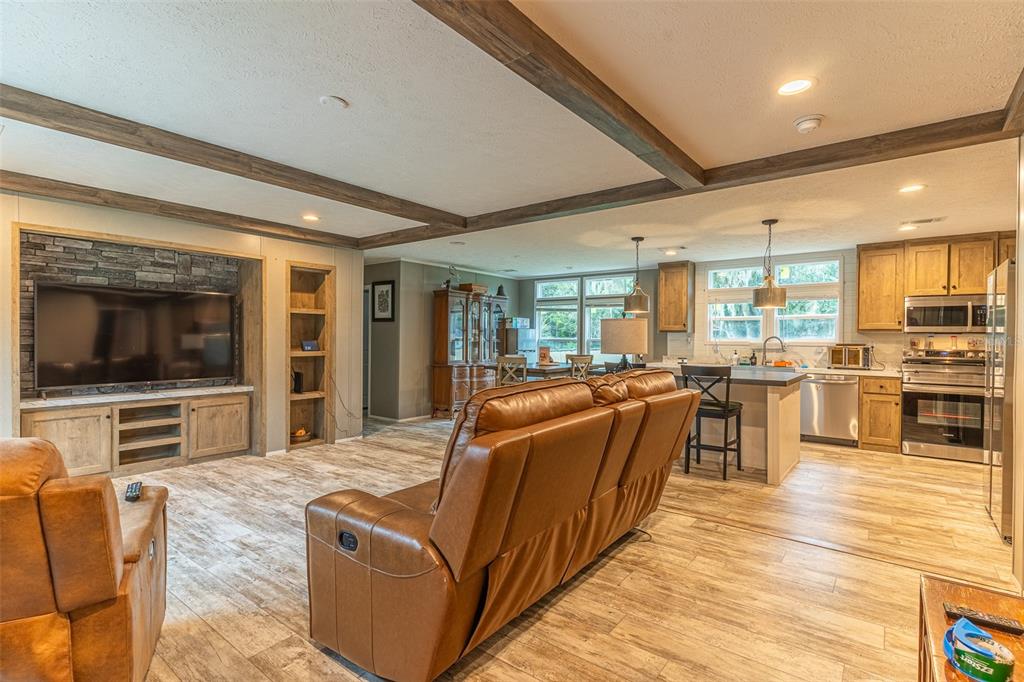 An open-concept living room and kitchen featuring wood-look flooring, exposed ceiling beams, and stone accents — 6668 CAIN STREET, MULBERRY, FL