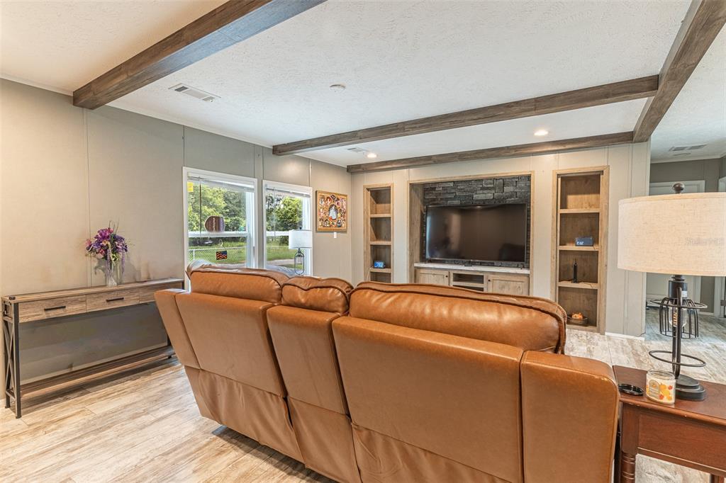 A living room features a brown leather sofa, wood-look flooring, ceiling beams, and a stone fireplace — 6668 CAIN STREET, MULBERRY, FL