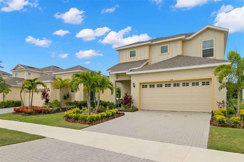 A two-story suburban house with a beige exterior, a two-car garage, and palm tree landscaping — 308 SHORE CRAB WAY, APOLLO BEACH, FL