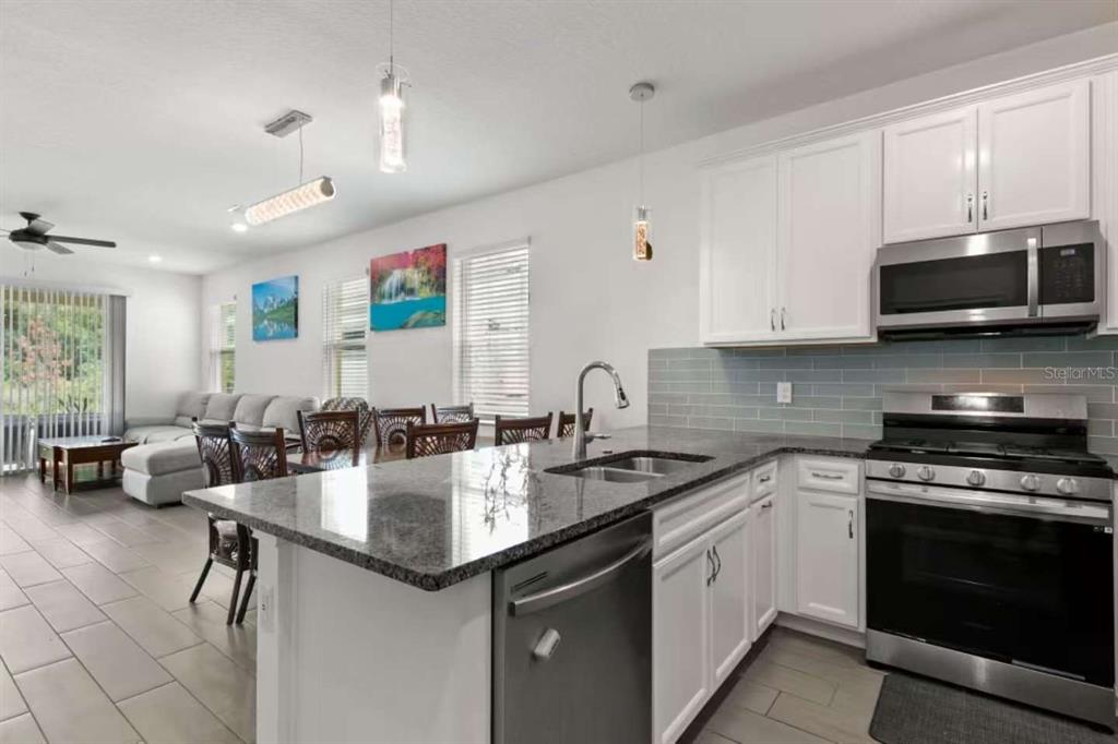 A kitchen with white cabinets, granite countertops, and stainless steel appliances overlooks an open living area — 308 SHORE CRAB WAY, APOLLO BEACH, FL