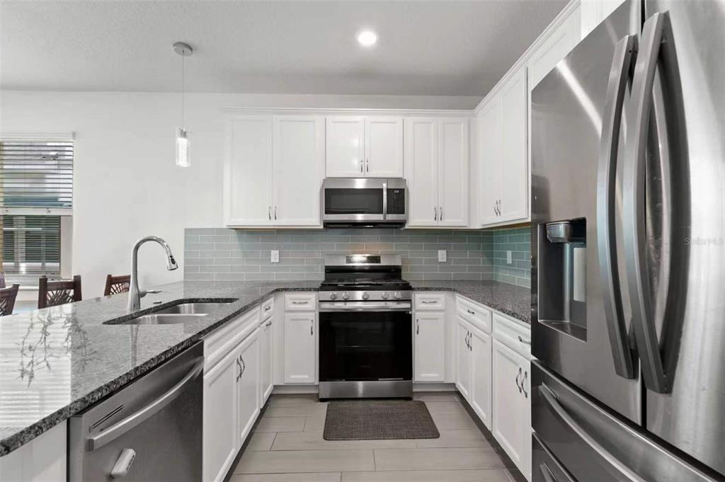 A kitchen features white cabinets, granite countertops, stainless steel appliances, and a gray tile backsplash — 308 SHORE CRAB WAY, APOLLO BEACH, FL