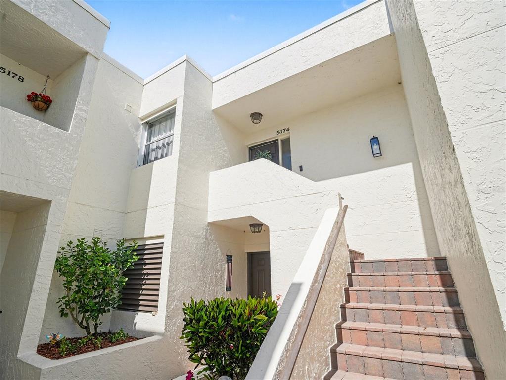 A two-story stucco building exterior features a staircase leading to an upper-level entrance — 5174 MARSH FIELD LANE UNIT 86, SARASOTA, FL