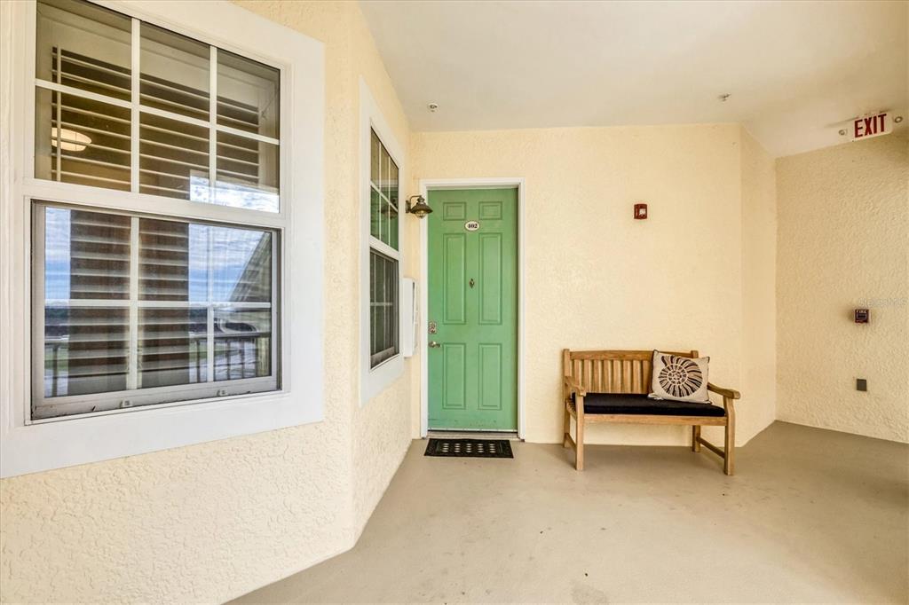 A covered exterior entryway features a green front door, a wooden bench, and windows — 8571 AMBERJACK CIRCLE UNIT 402, ENGLEWOOD, FL