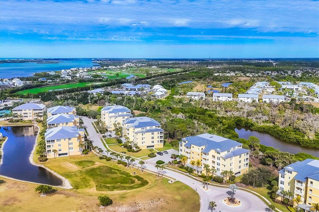 An aerial view shows several multi-story apartment buildings surrounded by green space and water — 8571 AMBERJACK CIRCLE UNIT 402, ENGLEWOOD, FL