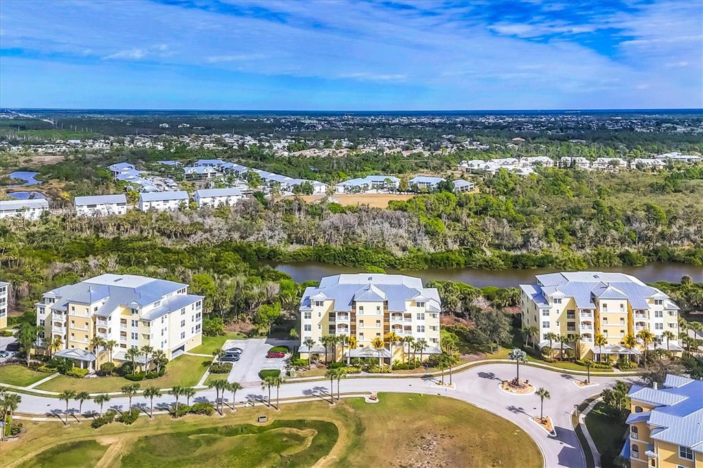An aerial view shows three multi-story apartment buildings situated near a river and greenery — 8571 AMBERJACK CIRCLE UNIT 402, ENGLEWOOD, FL
