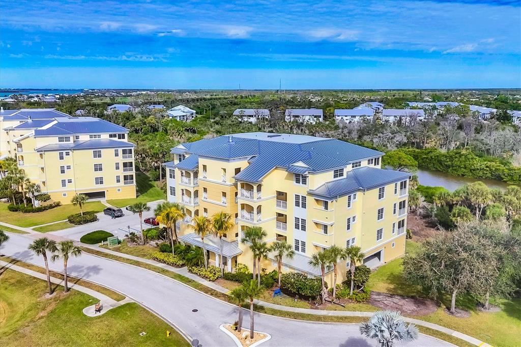 An aerial view of a multi-story yellow apartment building with a blue metal roof — 8571 AMBERJACK CIRCLE UNIT 402, ENGLEWOOD, FL
