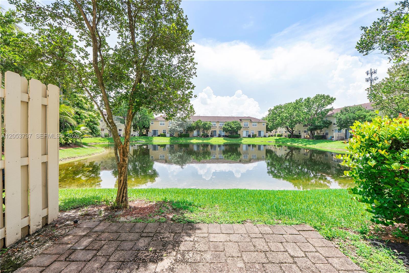 A paved patio overlooks a small pond surrounded by grass, trees, and apartment buildings — 2851 W Prospect Rd # 1307, Tamarac FL 33309, TAMARAC, FL