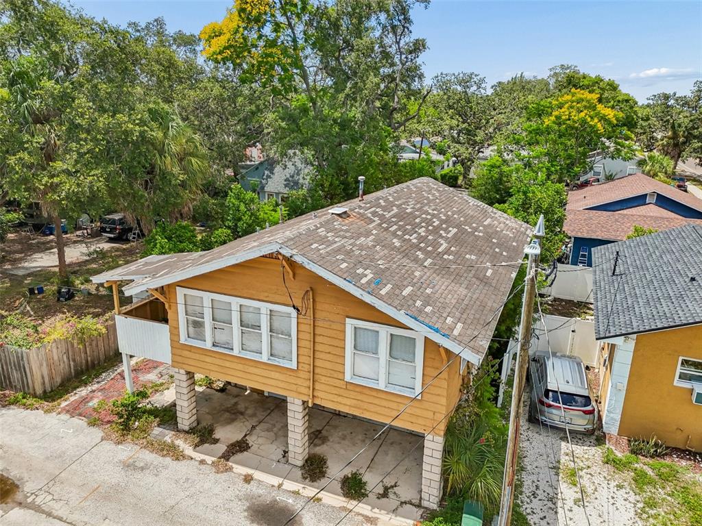 An elevated yellow house with a weathered roof sits above a concrete block parking area — 2210 20TH AVENUE S, ST PETERSBURG, FL