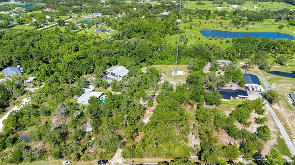 An aerial view shows a wooded property featuring several houses, outbuildings, and a tall radio tower — 1835 S GLENCOE ROAD, NEW SMYRNA BEACH, FL