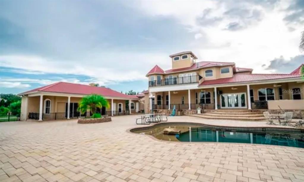 A large house with a red metal roof, a pool, and a paved patio area — 11715 TAYLOR ROAD, THONOTOSASSA, FL