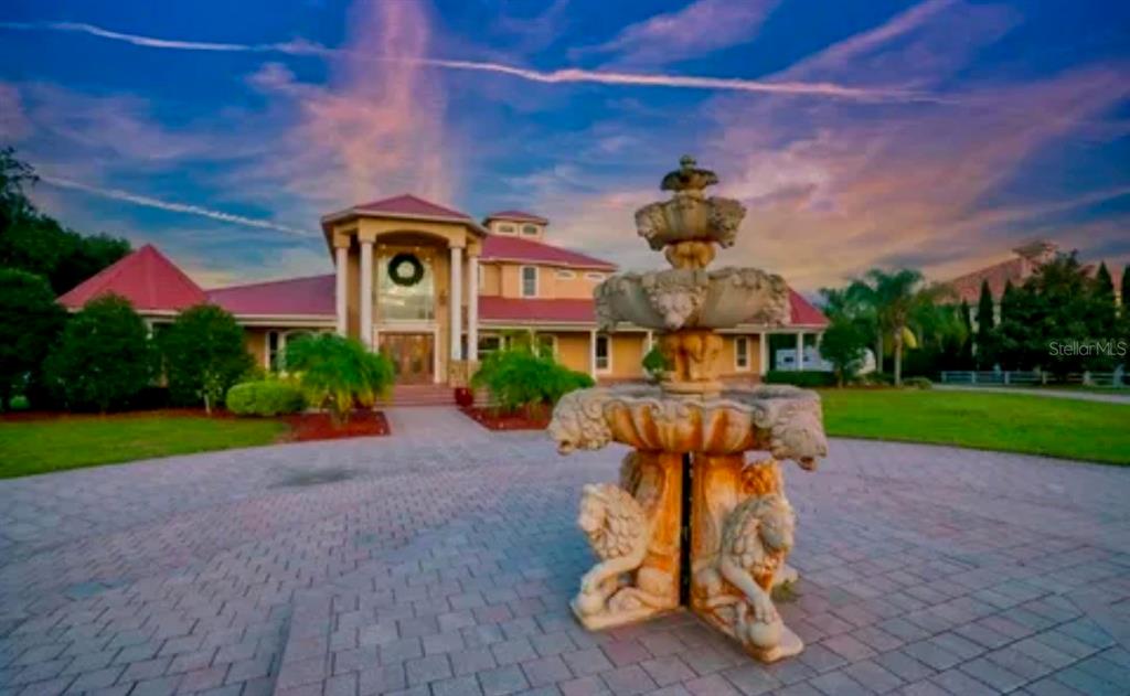 A tiered stone fountain stands in the foreground of a large house with a circular driveway — 11715 TAYLOR ROAD, THONOTOSASSA, FL