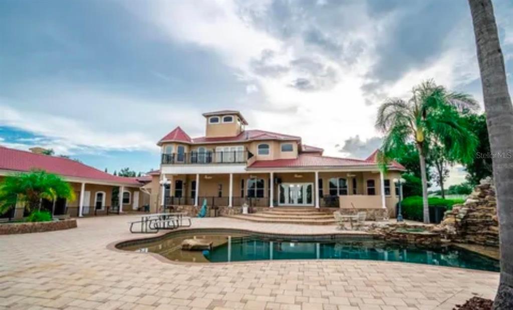 A large multi-story house with a red metal roof overlooks a backyard swimming pool — 11715 TAYLOR ROAD, THONOTOSASSA, FL