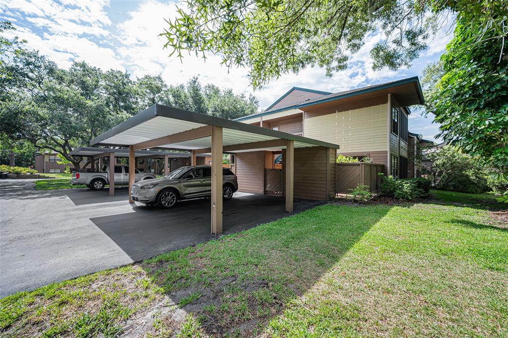 A two-story apartment building with a covered carport and parked vehicles on a sunny day — 2205 LENNOX ROAD E UNIT 2205, PALM HARBOR, FL