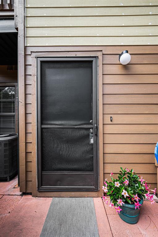 A dark metal screen door is centered on a brown wood-paneled exterior wall — 2205 LENNOX ROAD E UNIT 2205, PALM HARBOR, FL