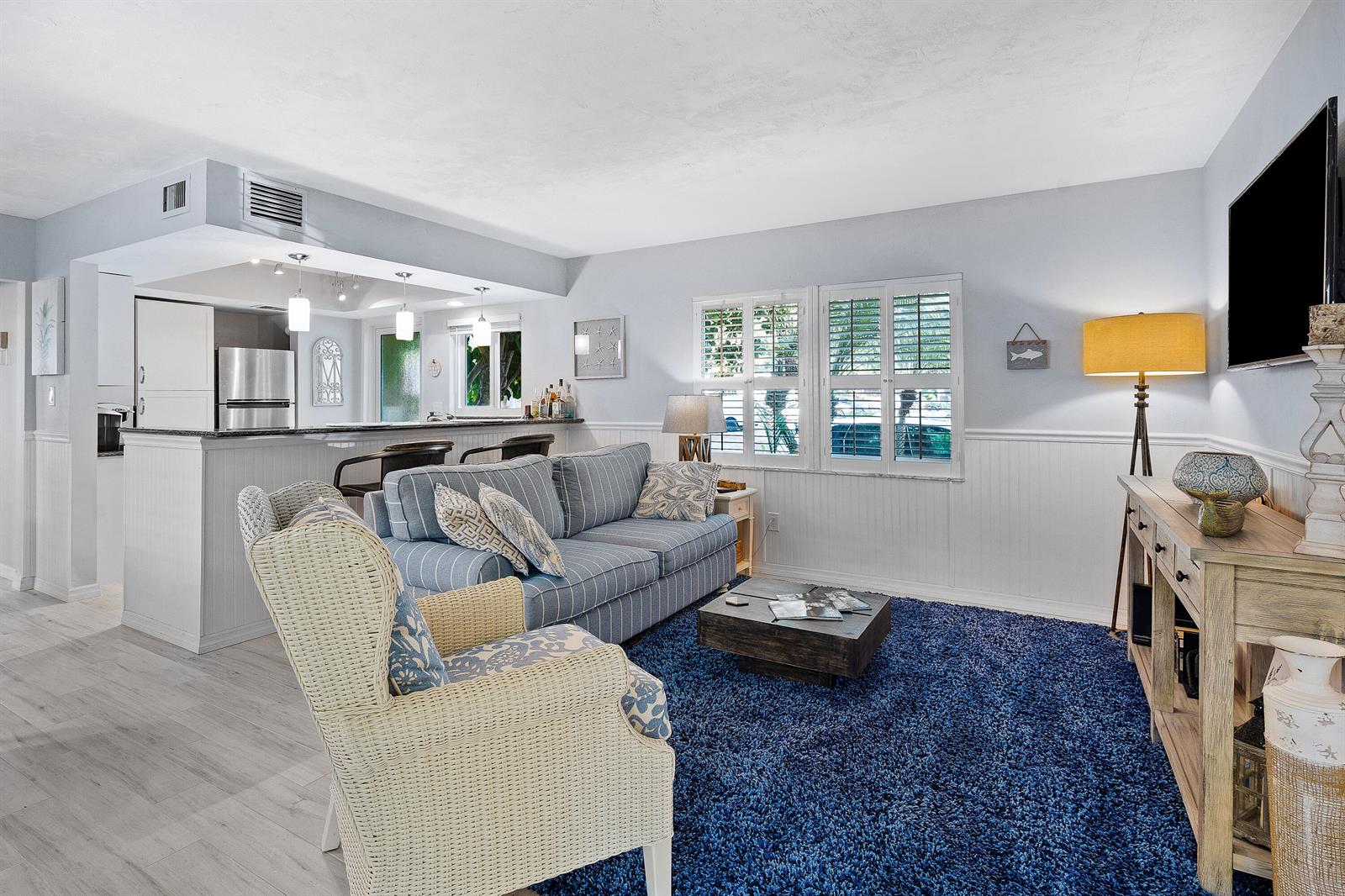 A living room features a blue striped sofa, wicker armchair, and a dark blue rug — 1030 Langer Way # 5, Delray Beach FL 33483, DELRAY BEACH, FL