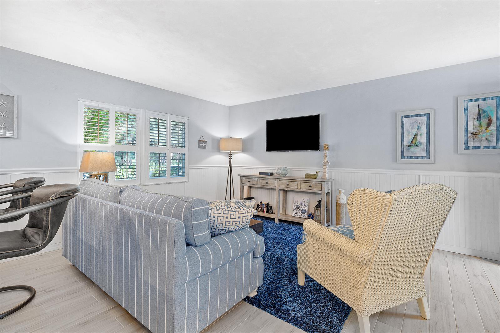 A living room features a striped sofa, wicker chair, blue rug, and wall-mounted television — 1030 Langer Way # 5, Delray Beach FL 33483, DELRAY BEACH, FL