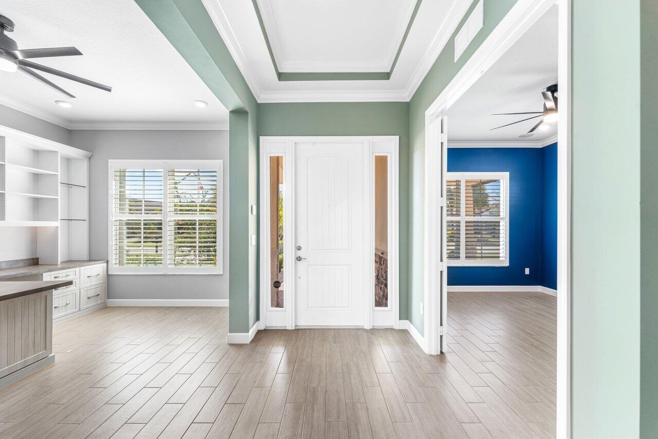 An entryway with light wood flooring, sage green walls, and a white front door — 940 Hookline Circle, Loxahatchee FL 33470, LOXAHATCHEE, FL
