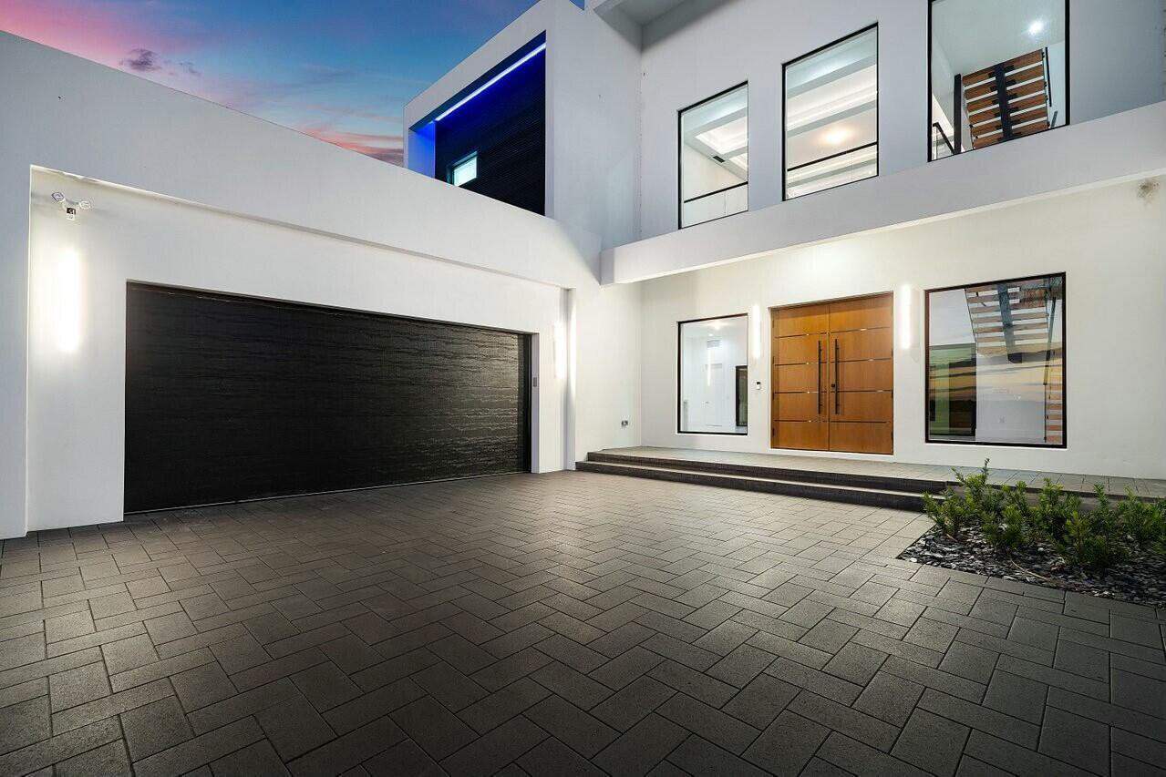 A modern two-story house exterior features a black garage door, wood front doors, and pavers — 13440 Us Highway 1, Juno Beach FL 33408, JUNO BEACH, FL