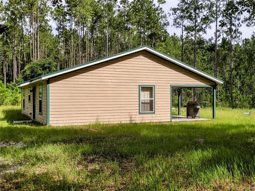 A tan, single-story house with a green-trimmed porch and a grill sits in a forest — 4651 NE 108TH PLACE, CHIEFLAND, FL