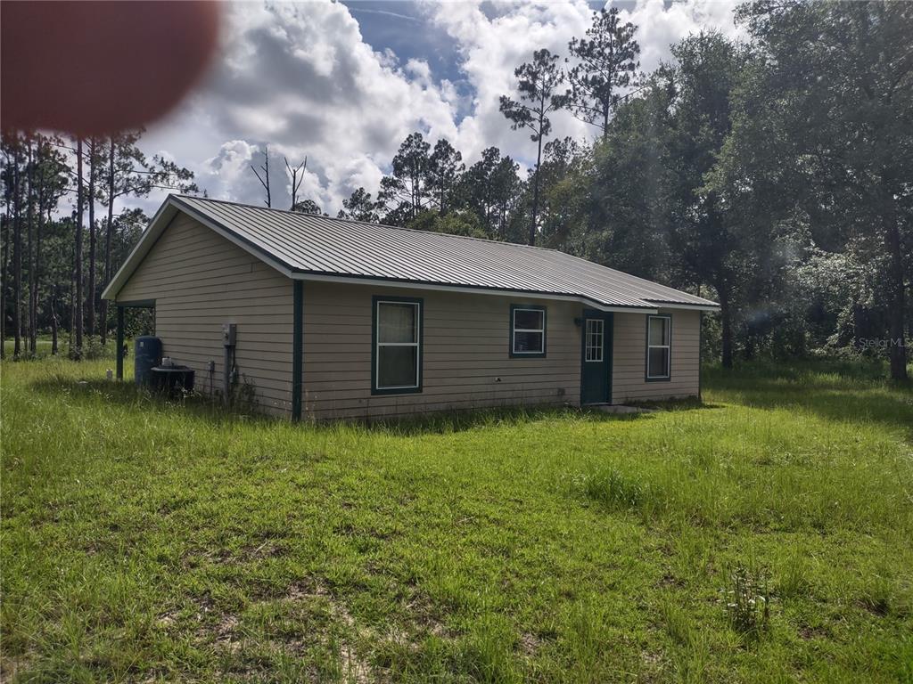 A single-story house with tan siding and a metal roof sits in a grassy field — 4651 NE 108TH PLACE, CHIEFLAND, FL
