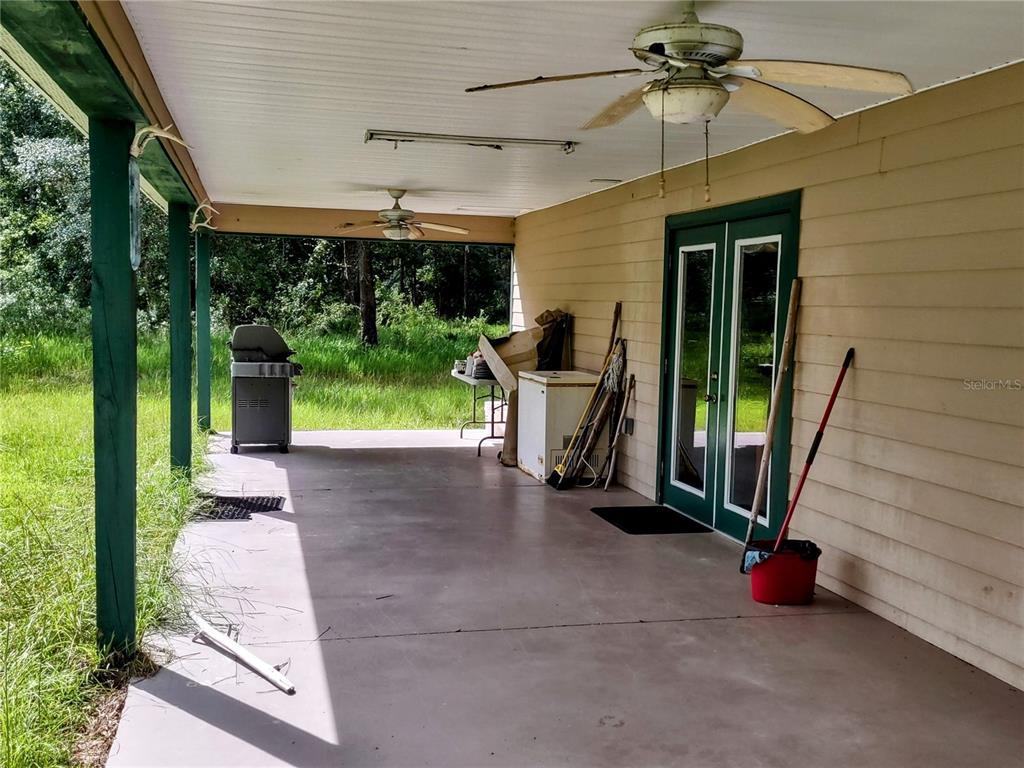 A covered concrete patio features a ceiling fan, a grill, a chest freezer, and double doors — 4651 NE 108TH PLACE, CHIEFLAND, FL