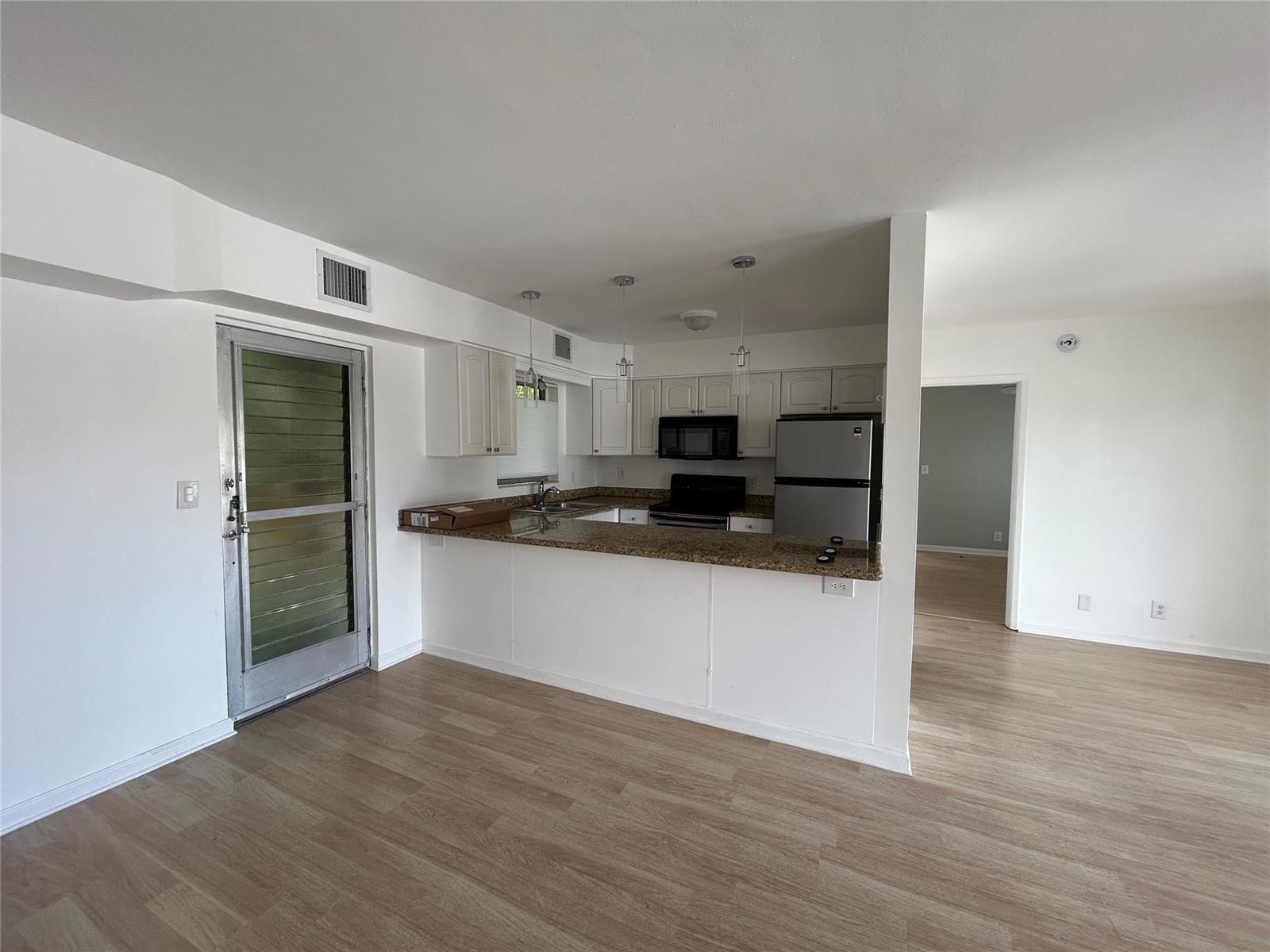 A kitchen with white cabinets, granite countertops, and stainless steel appliances opens to a living area — 77 Hendricks Isle # 10, Fort Lauderdale FL 33301, FORT LAUDERDALE, FL